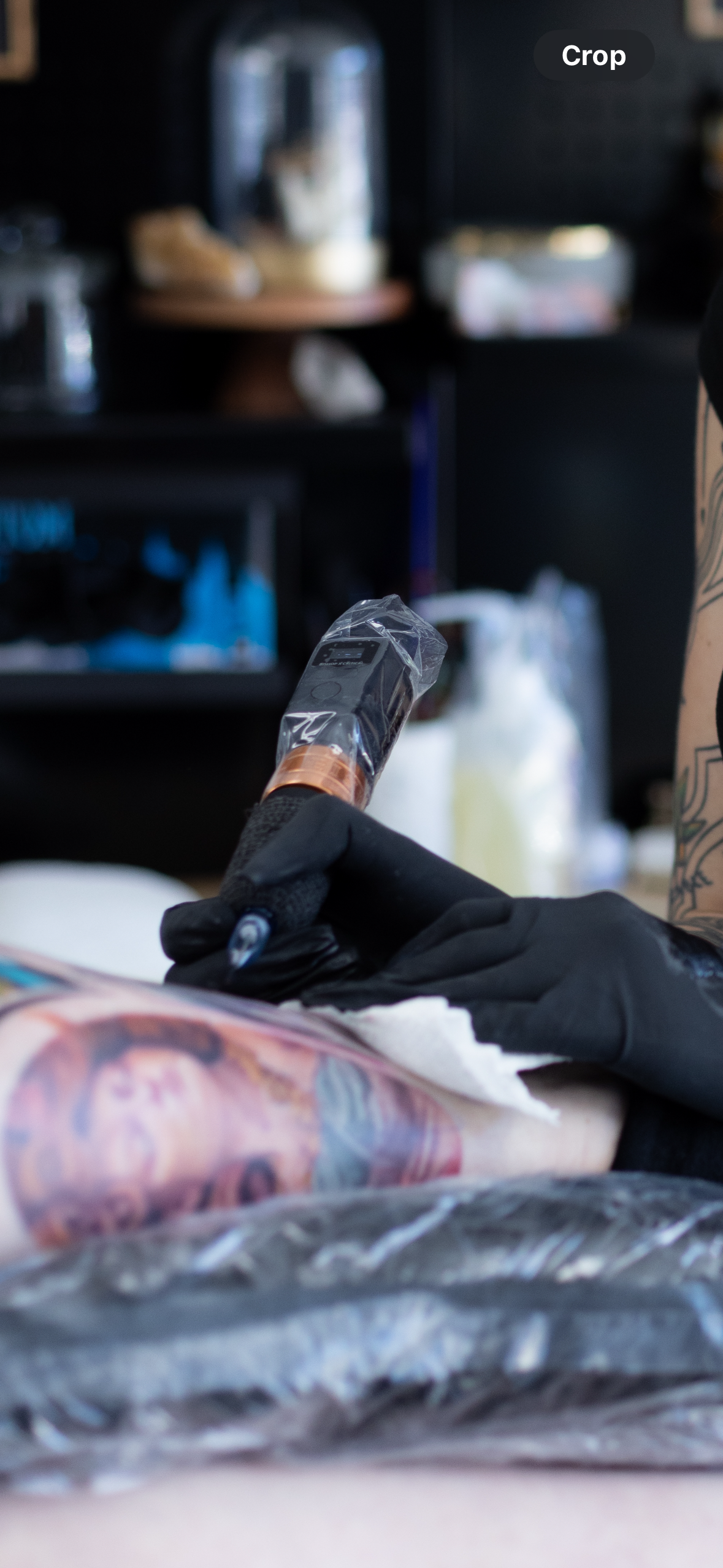 Tattoo artist using a tattoo machine on a person's arm with a colorful portrait tattoo.
